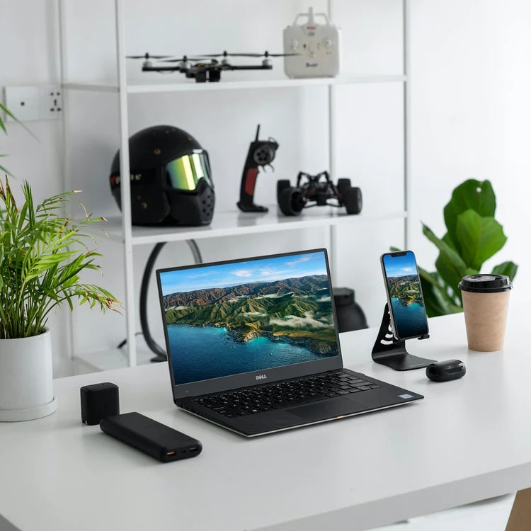 una mesa blanca con una computadora, un casco, un dron, un café y un teléfono